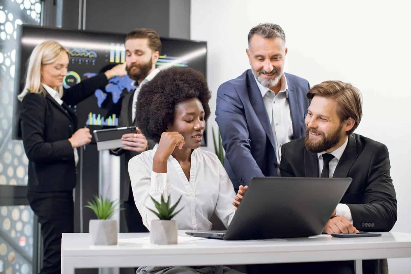 Front view of pleasant happy confident mixed race business colleagues, african lady and two caucasian men, working together over joint project on laptop. man and woman standing on the background