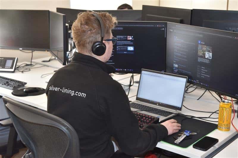 IT support technician wearing a headset working across multiple monitors and a laptop, providing responsive helpdesk support and inbound calling.