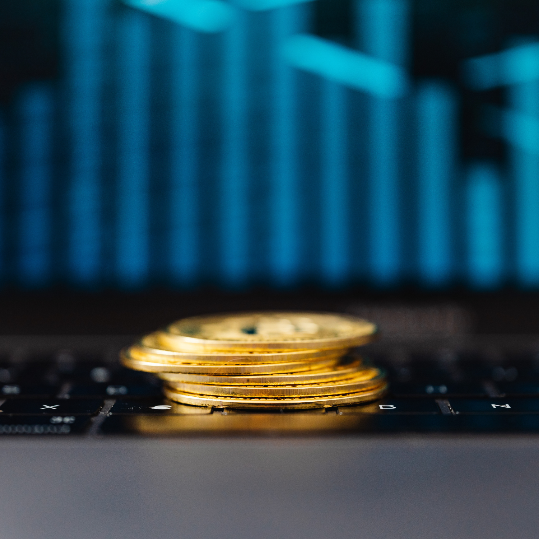 A stack of gold coins on a laptop keyboard with blurred digital data in the background, representing investment in cyber security and protecting business systems.